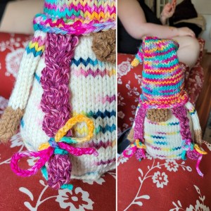 A knitted gnome with a pink/yellow/turquoise knit cap, pink cabled hair, a brown nose and cream body.